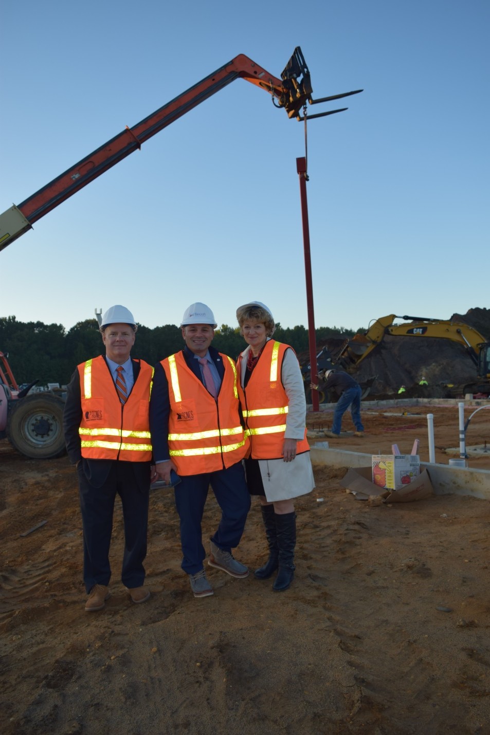 three Bancroft employees stand at a construction site wearing bright orange vests