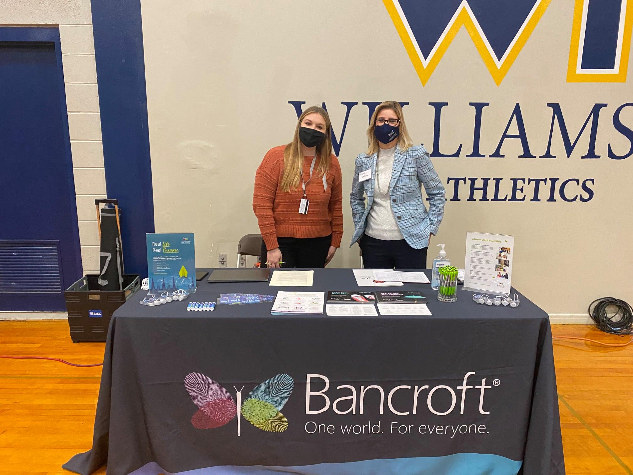 Two members of Bancroft's team of Talent Acquisition Partners standing in front of table with a Bancroft table cover on it.